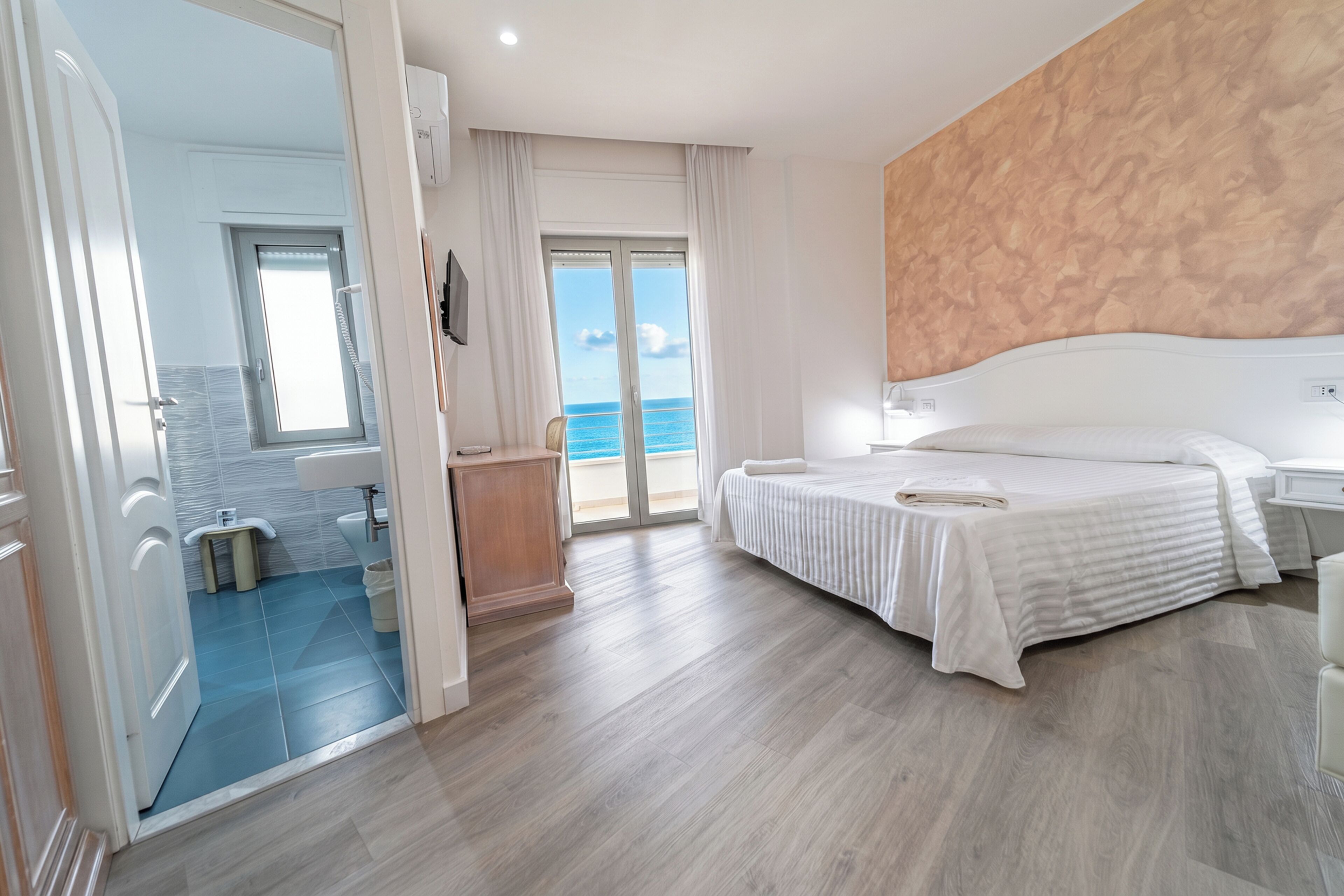 A hotel room with a bed, a bathroom, and a view of the sea.