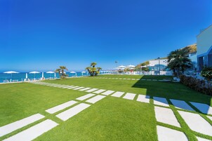 A well-maintained lawn with a clear view of the ocean, a pool area with umbrellas, and a building with a modern design.