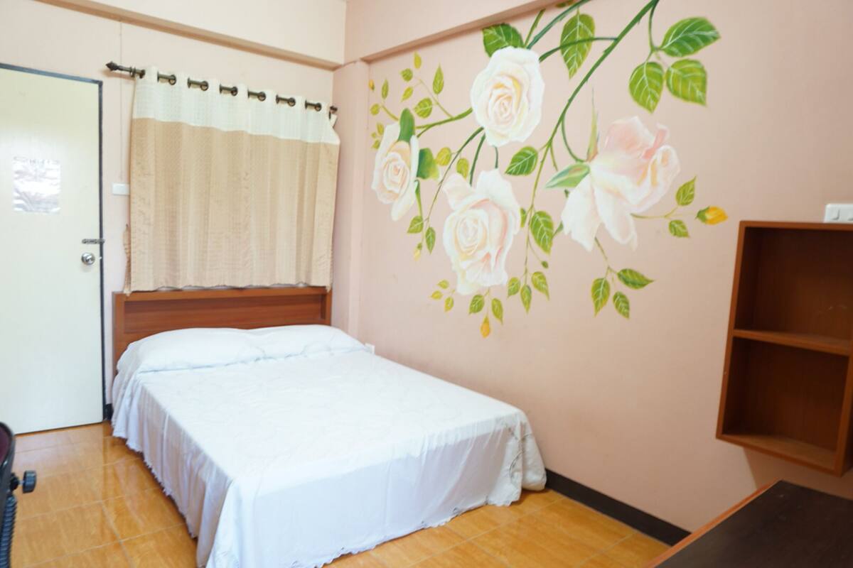 A bedroom with a bed, a wooden headboard, a wall with a floral mural, a wooden shelf, and a door with a curtain.