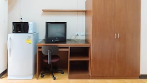 A compact room with a wooden desk, a computer, a white refrigerator, and a wooden wardrobe. - Chiang Mai Tree Hostel (Chiang Mai)