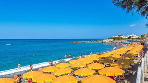A beach with numerous yellow umbrellas, people sunbathing, and a clear blue sky.