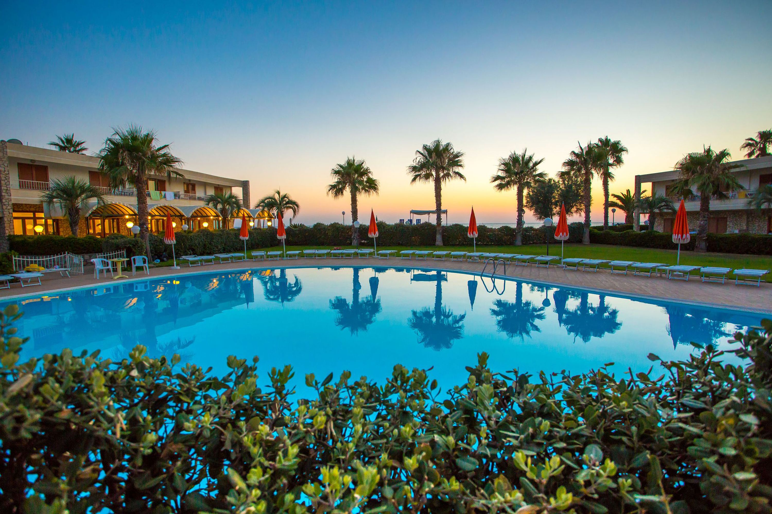 A swimming pool with palm trees and lounge chairs, surrounded by hotel buildings.