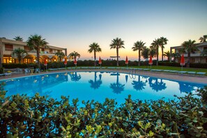 Una piscina con palmeras y sillas de descanso, rodeada de edificios de hotel.