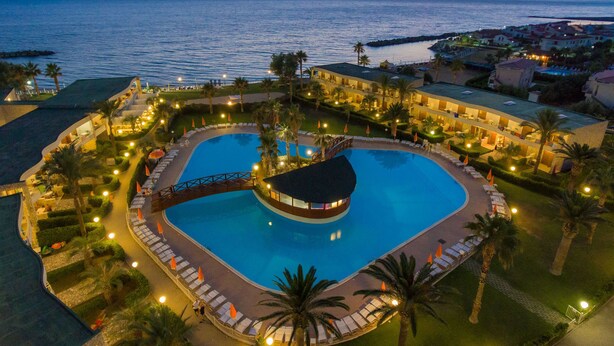 A resort with a large central pool, multiple guest rooms, and a view of the sea.