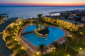 Un resort con una amplia piscina central, numerosas habitaciones e vistas al mar.