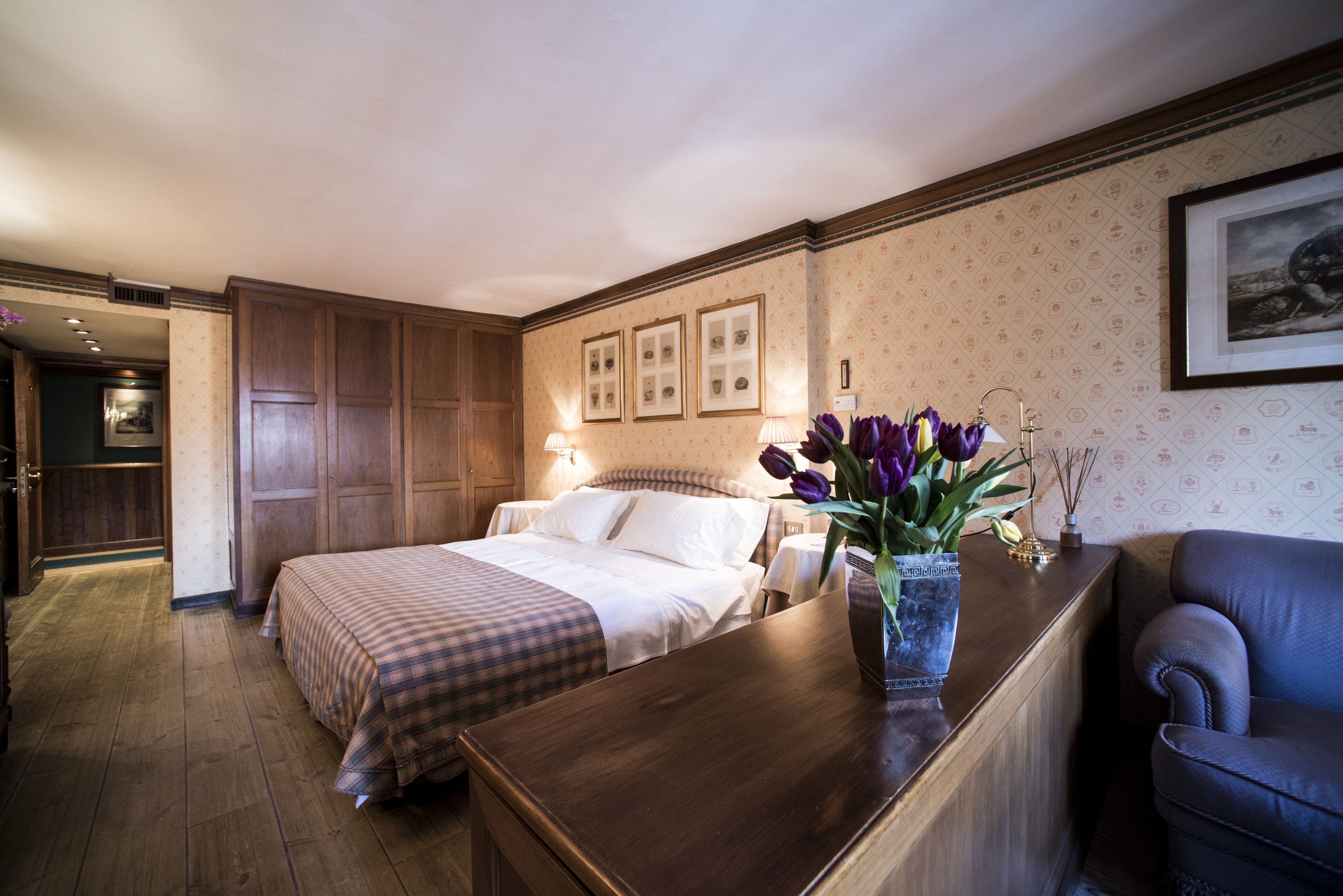 Ein Hotelzimmer mit einem großen Bett, einem Holztisch, einem Stuhl und einer Vase mit Blumen.