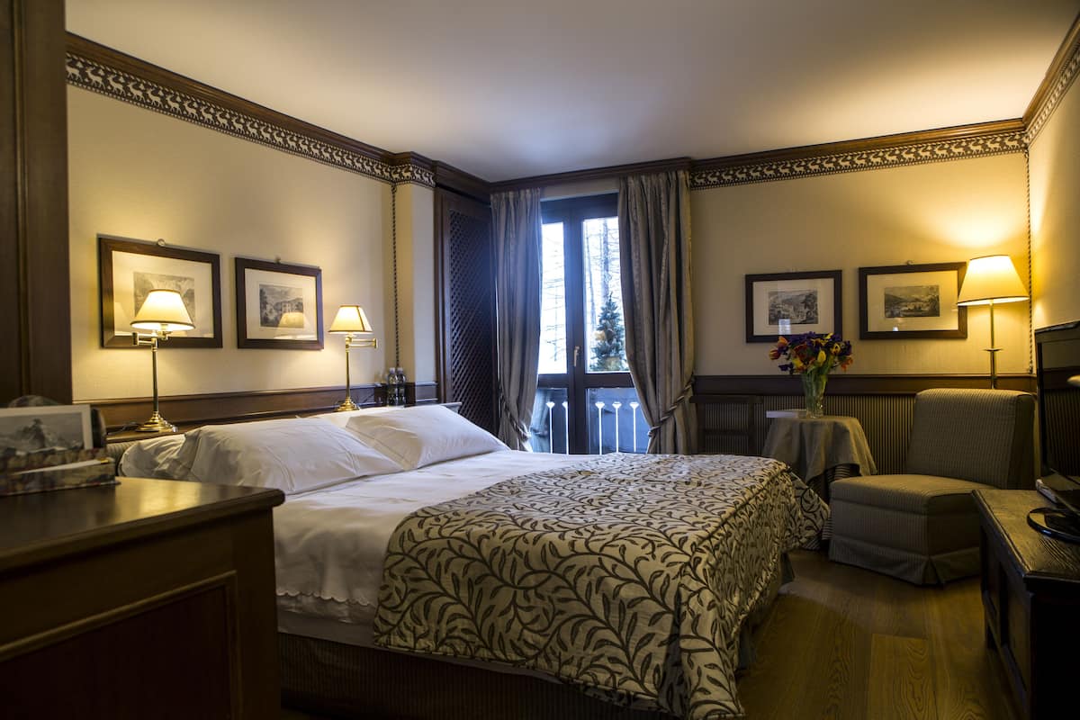 Una habitación de hotel con una cama grande, dos mesitas de noche, una silla, un escritorio y una ventana con cortinas.