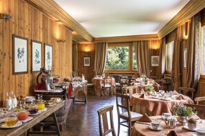 A dining area with wooden paneling, tables set for a meal, and framed artwork on the walls. - Hermitage Hotel (Valtournenche)