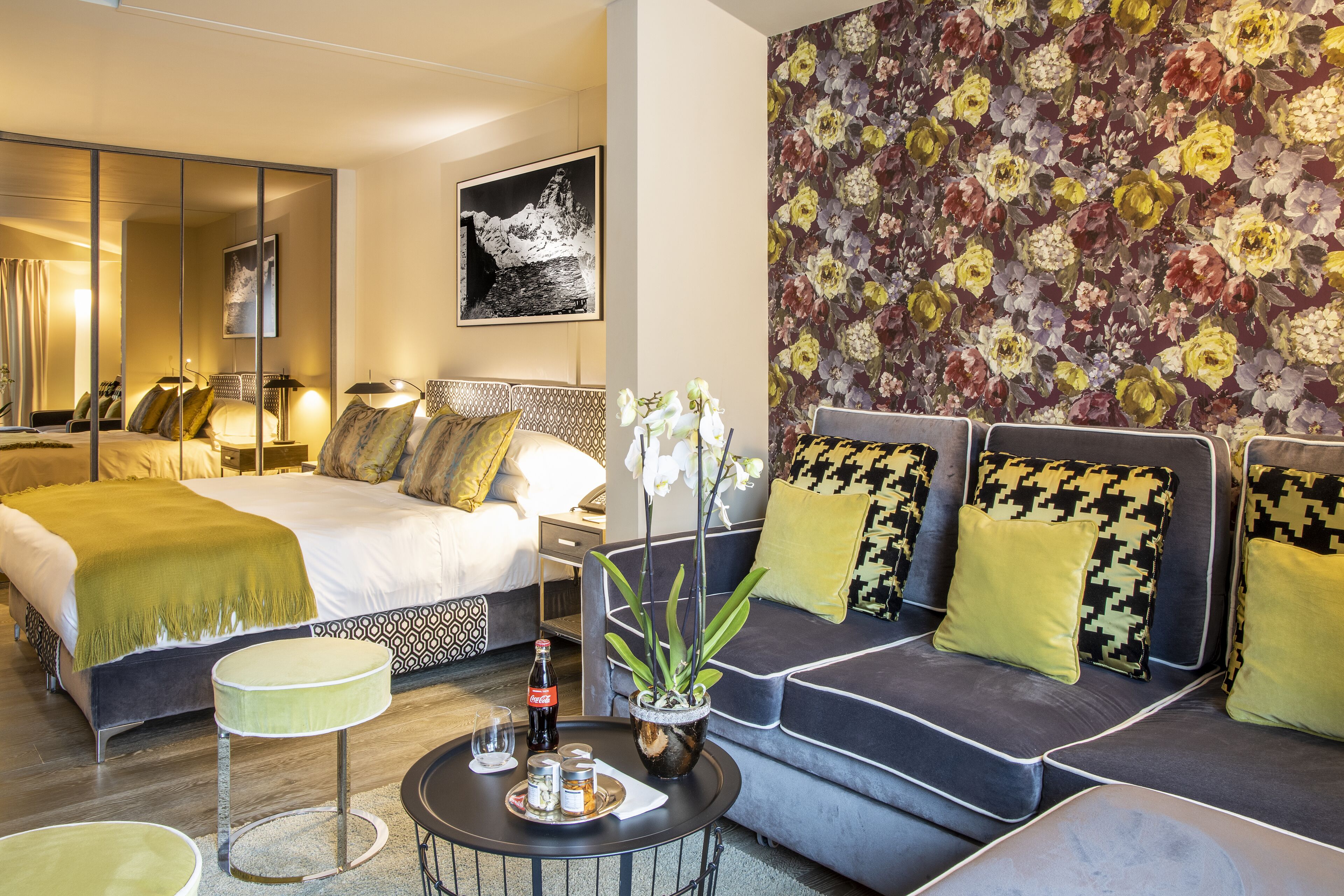 Une chambre d’hôtel moderne avec un grand lit, un canapé, une petite table ronde et un papier peint à motifs floraux.
