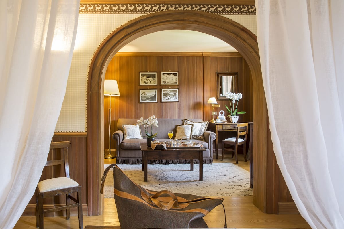 Un salón acogedor con un arco de madera, un sofá, una mesa de centro y una silla. Hay cuadros en la pared y un jarrón con flores sobre la mesa de centro.