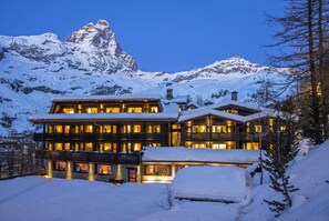 Un hotel de varios pisos con balcones y montañas al fondo.