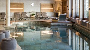 A modern indoor pool area with lounge chairs, a stone wall, and large windows. - Hermitage Hotel (Valtournenche)