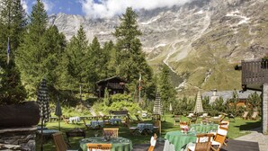 An outdoor dining area with tables and chairs, surrounded by trees and mountains in the background. - Hermitage Hotel (Valtournenche)