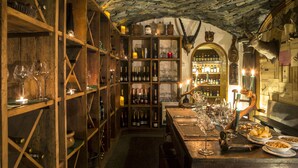 A wine cellar with wooden shelves, wine bottles, and glasses. - Hermitage Hotel (Valtournenche)