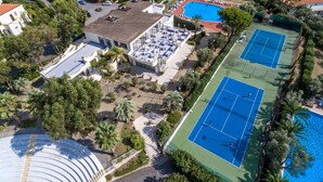 An aerial view of a residential area with a swimming pool, tennis courts, and a large building with a sloped roof.