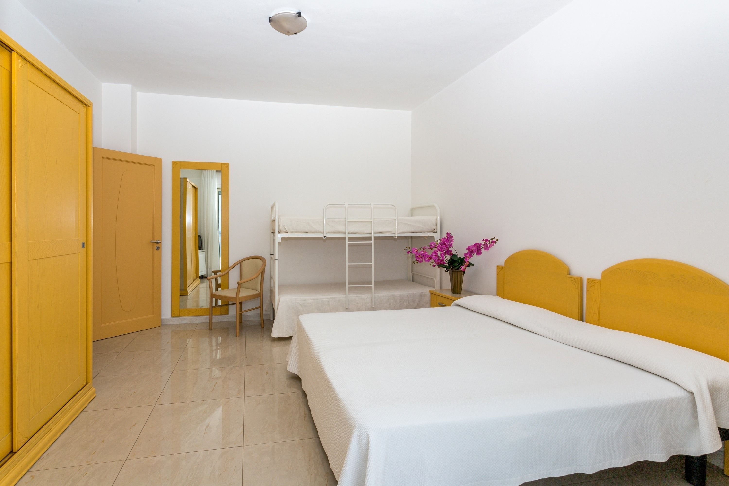 A room with a bunk bed, a single bed, a chair, and a mirror.