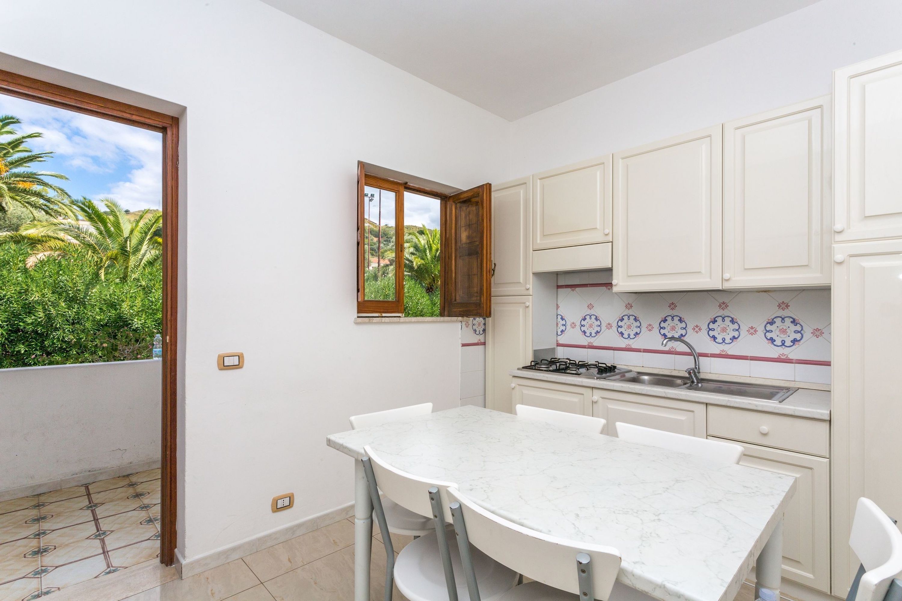 A kitchen with white cabinets, a marble countertop, and a window overlooking greenery.