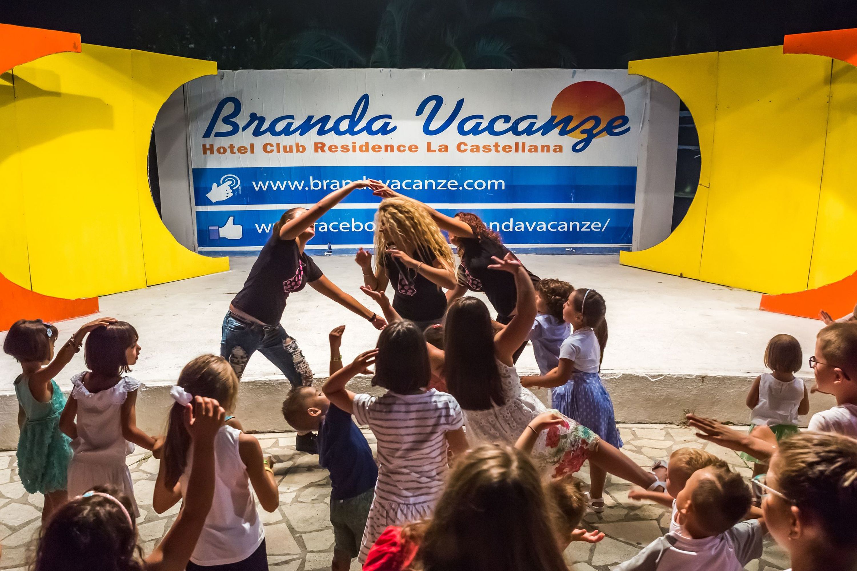 A group of children gathered in front of a sign for Branda Vacanze Hotel Club Residence La Castellana.