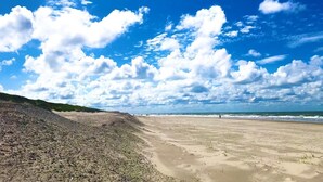 Uma praia com areal arenoso e um penhasco rochoso.