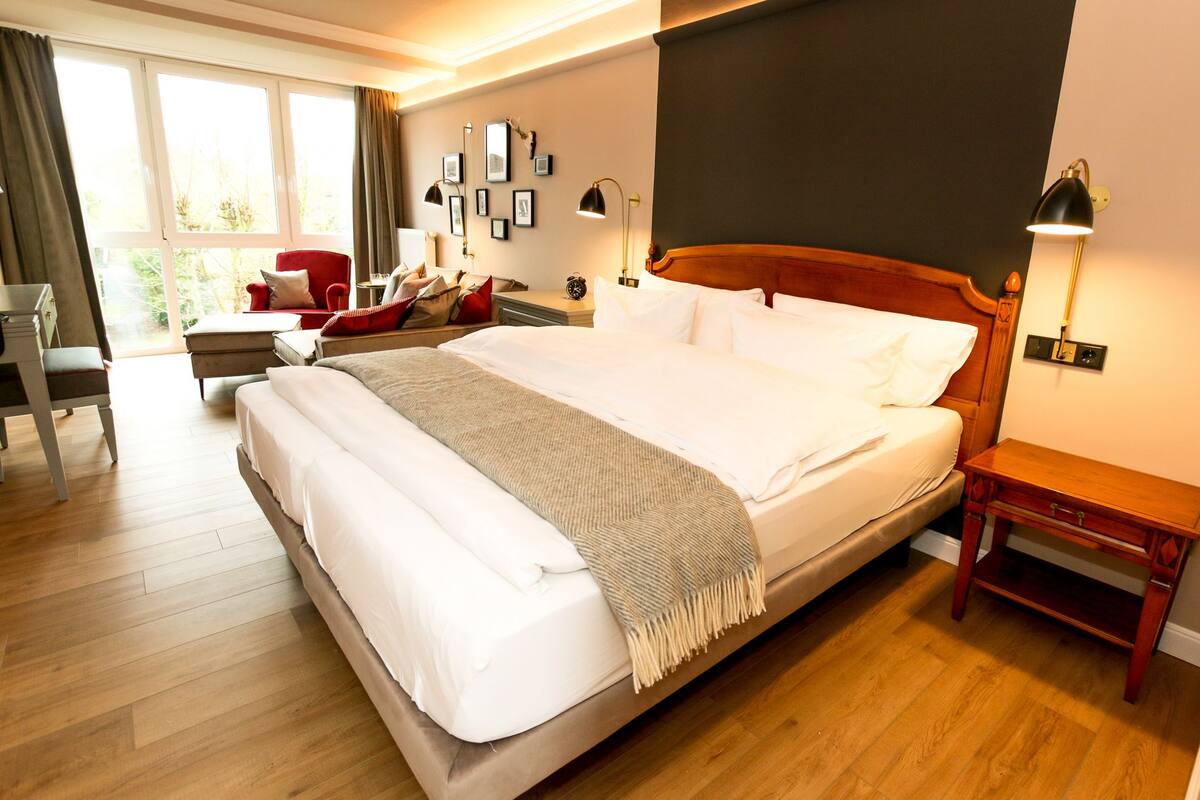 Une chambre bien éclairée, avec un grand lit, une table de chevet, une chaise et un bureau.