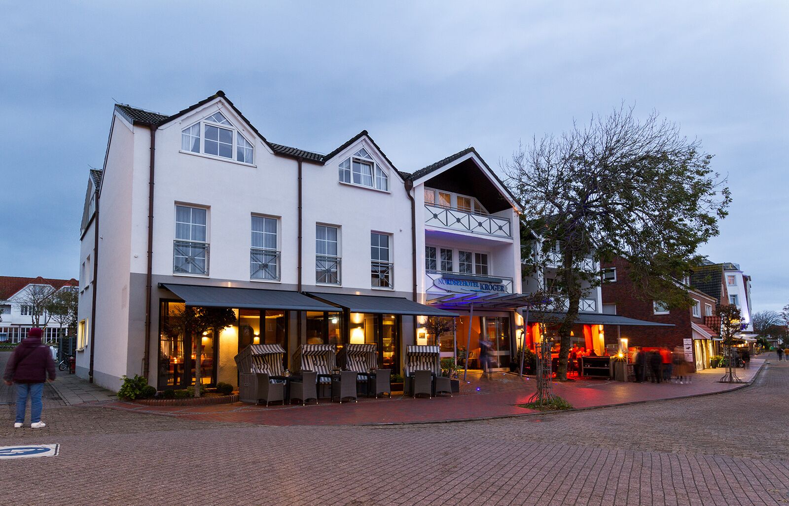 A hotel with a white facade, multiple windows, and outdoor seating.