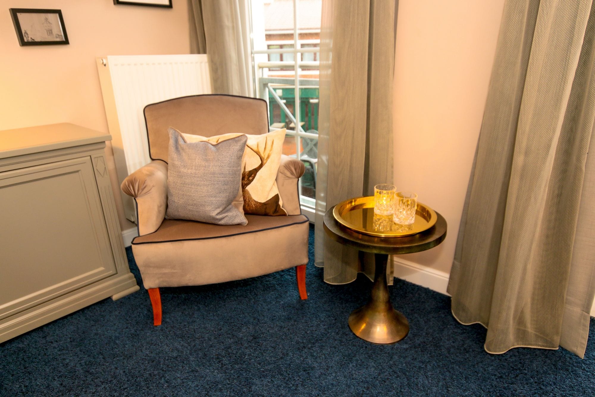 A room with a beige armchair, a small round table with a candle, and a window with curtains.
