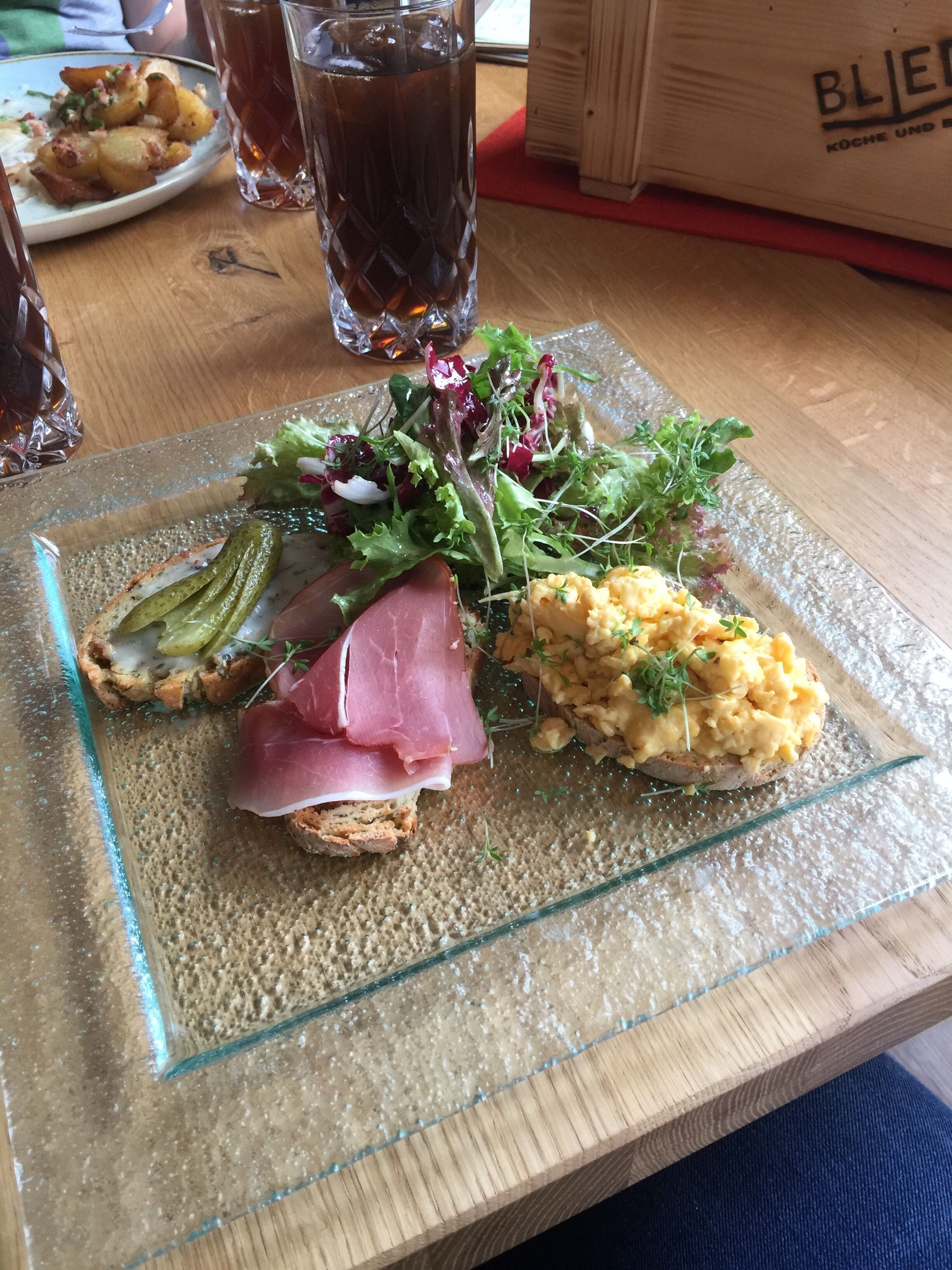 A meal with a variety of dishes including a salad, a meat dish, and a side of scrambled eggs on toast, served on a glass plate.