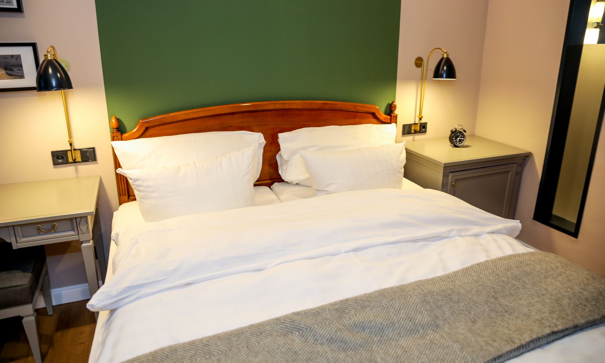 A neatly made bed with white linens, a wooden headboard, and two bedside lamps.