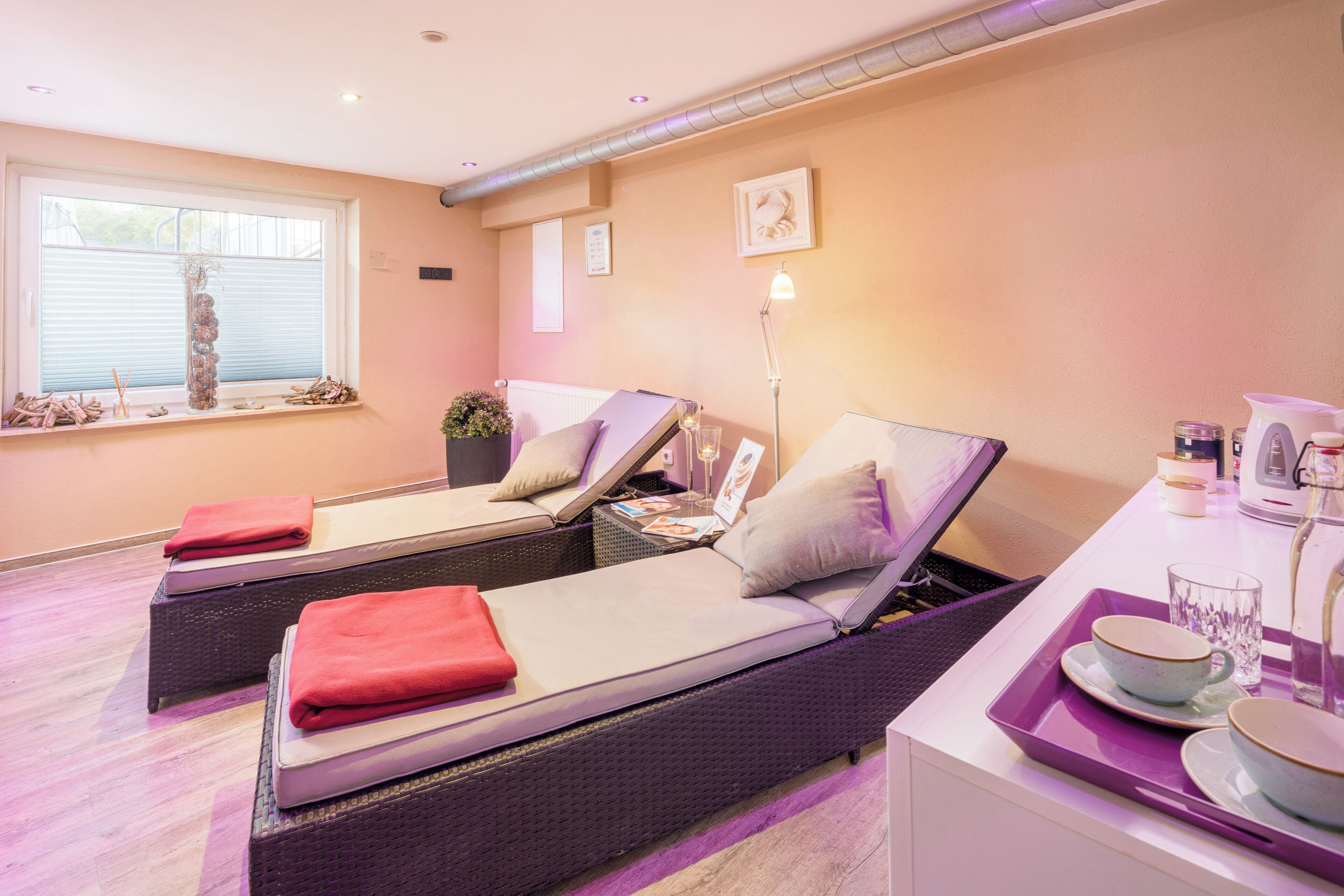 A room with two beds, a window with blinds, a bedside table with a lamp, and a tray with cups and a glass.