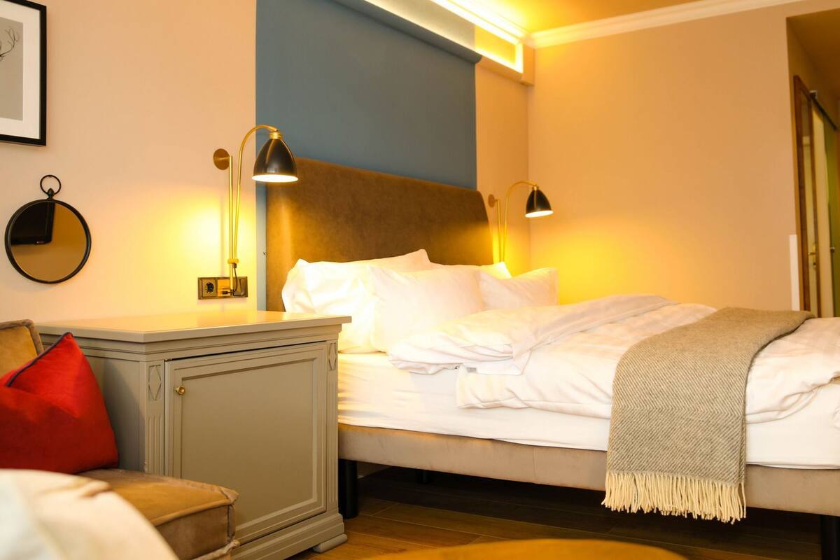 Un lit bien fait, avec une tête de lit, des lampes de chevet, un miroir et un oreiller rouge.