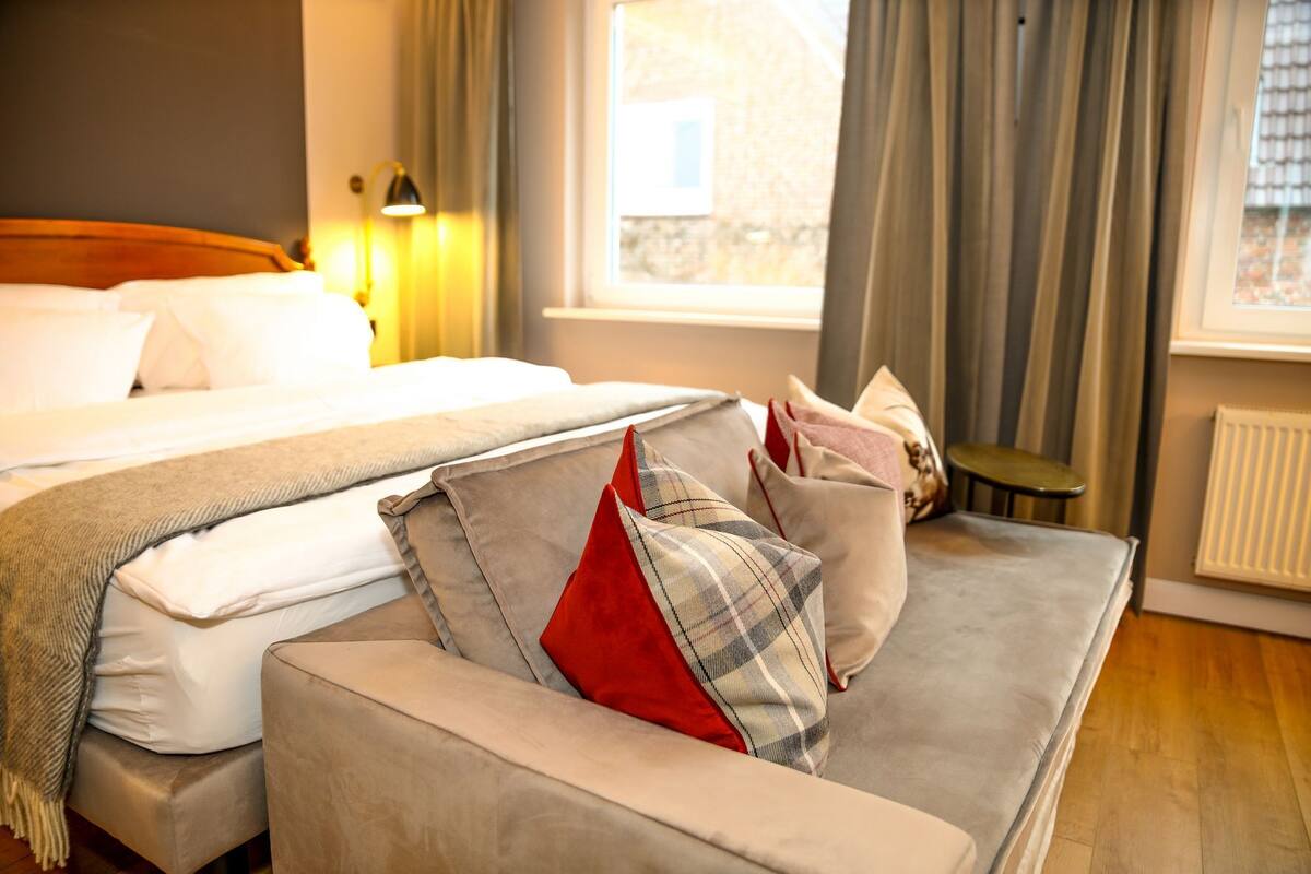 Une chambre d’hôtel avec un lit, un canapé, une petite table et une fenêtre avec des rideaux.