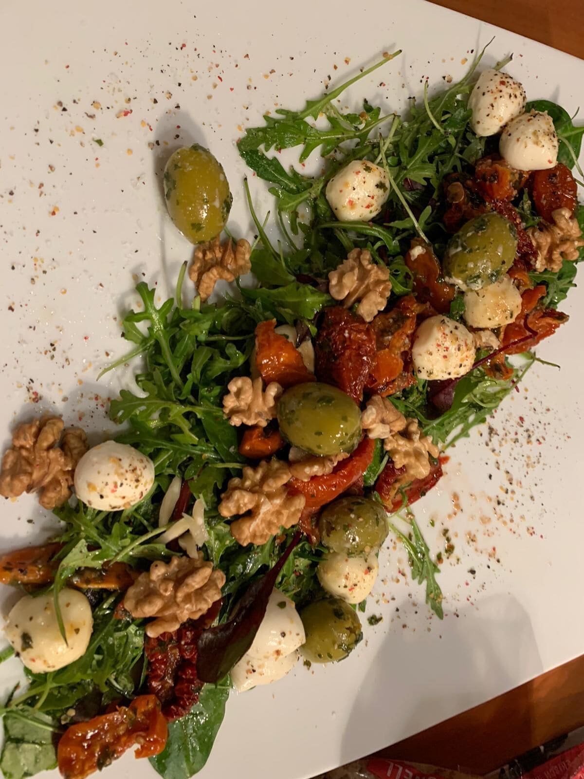 A white plate with a salad consisting of arugula, walnuts, cherry tomatoes, and mozzarella balls.