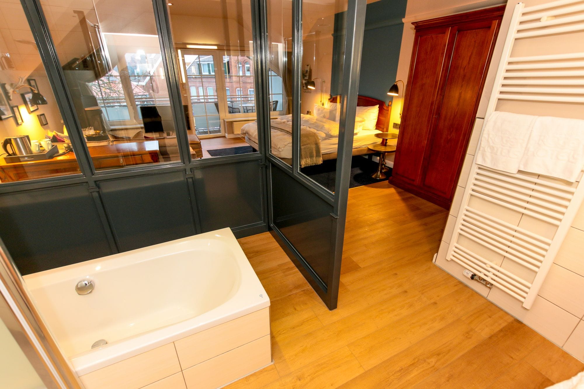 A modern bathroom with a bathtub, wooden flooring, and a glass shower enclosure.