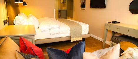 Une chambre d’hôtel comprenant un lit, une table de chevet, une lampe, une télévision et un bureau avec une chaise.