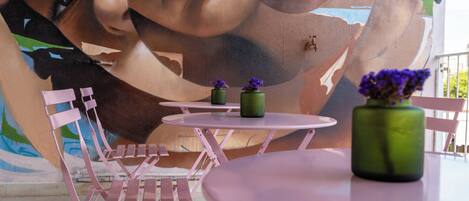 A dining area with pink chairs and tables, a mural with abstract art, and a green vase with purple flowers on a table.
