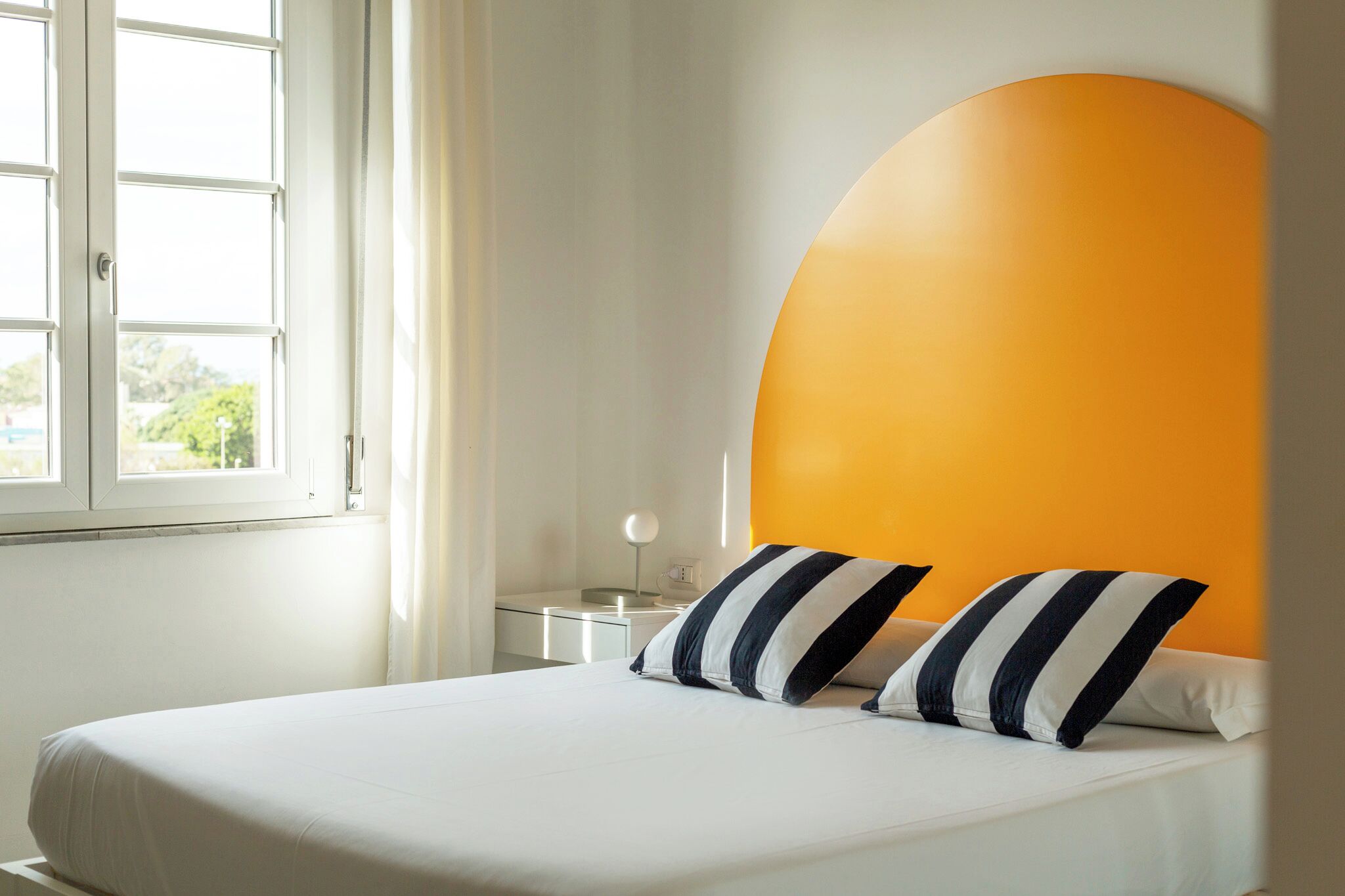 A hotel room with a bed, a nightstand, a lamp, and a window with curtains.