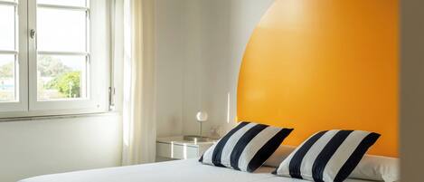 A hotel room with a bed, a nightstand, a lamp, and a window with curtains.