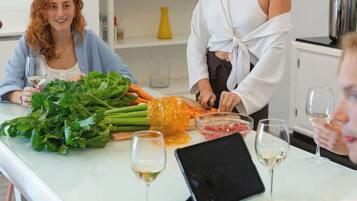 A group of people around a table with fresh vegetables, wine glasses, and a tablet.