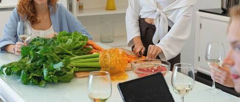 A group of people around a table with fresh vegetables, wine glasses, and a tablet.