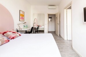 Ein modernes Schlafzimmer mit einem großen Bett, einem Schreibtisch mit Stuhl, einem Spiegel und einer Tür zu einem anderen Raum.