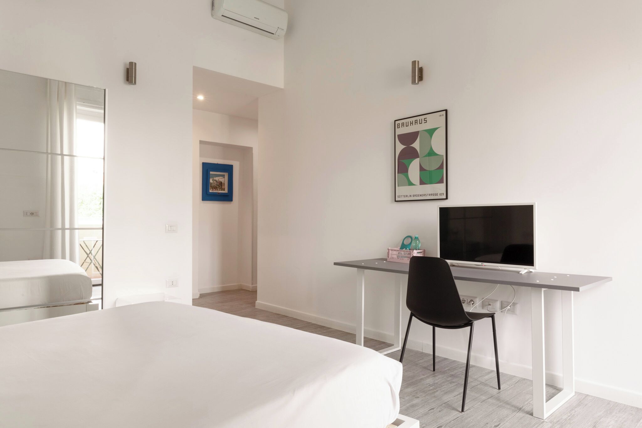 Habitació d'hotel moderna amb un llit, una taula de treball amb una cadira, una televisió i un quadre a la paret.
