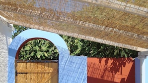 A wooden gate with a blue door, a white wall, and a red wall with a window. - Asteri Apartments (Alonissos)