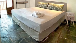 A bedroom with a large bed, a small table, a chair, and a door. - Asteri Apartments (Alonissos)