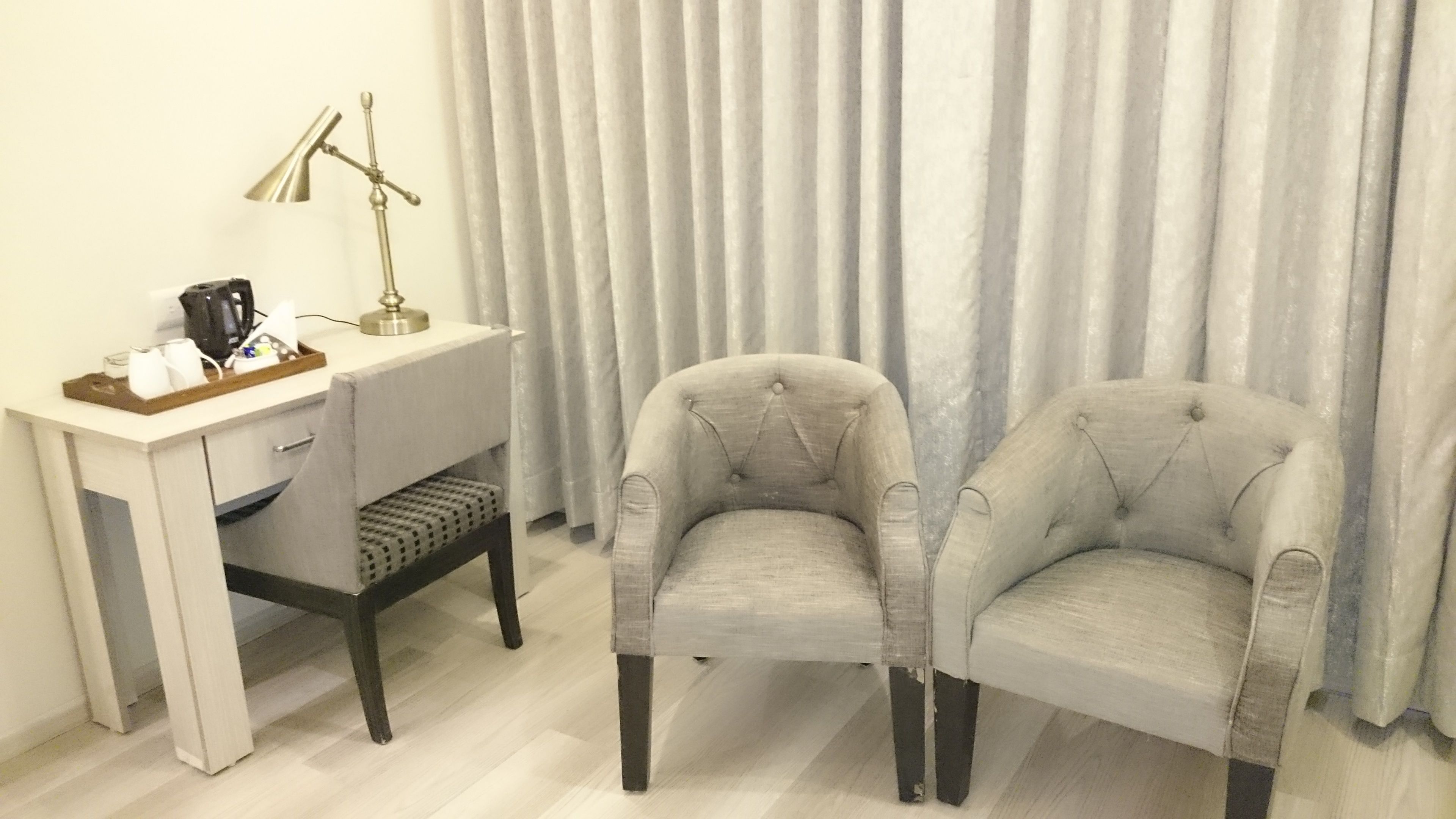 Una habitación con escritorio, dos sillones, una lámpara y un cortinero.