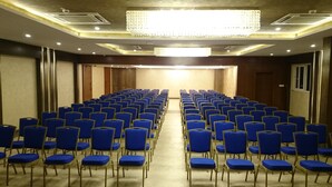 A conference room with rows of blue chairs and a chandelier. - Mango Hotels Naveen (Davanagere)