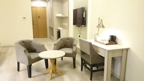 A small, modern room with a sofa, a round table, a desk with a chair, a flat-screen TV, and a coffee machine. - Mango Hotels Naveen (Davanagere)