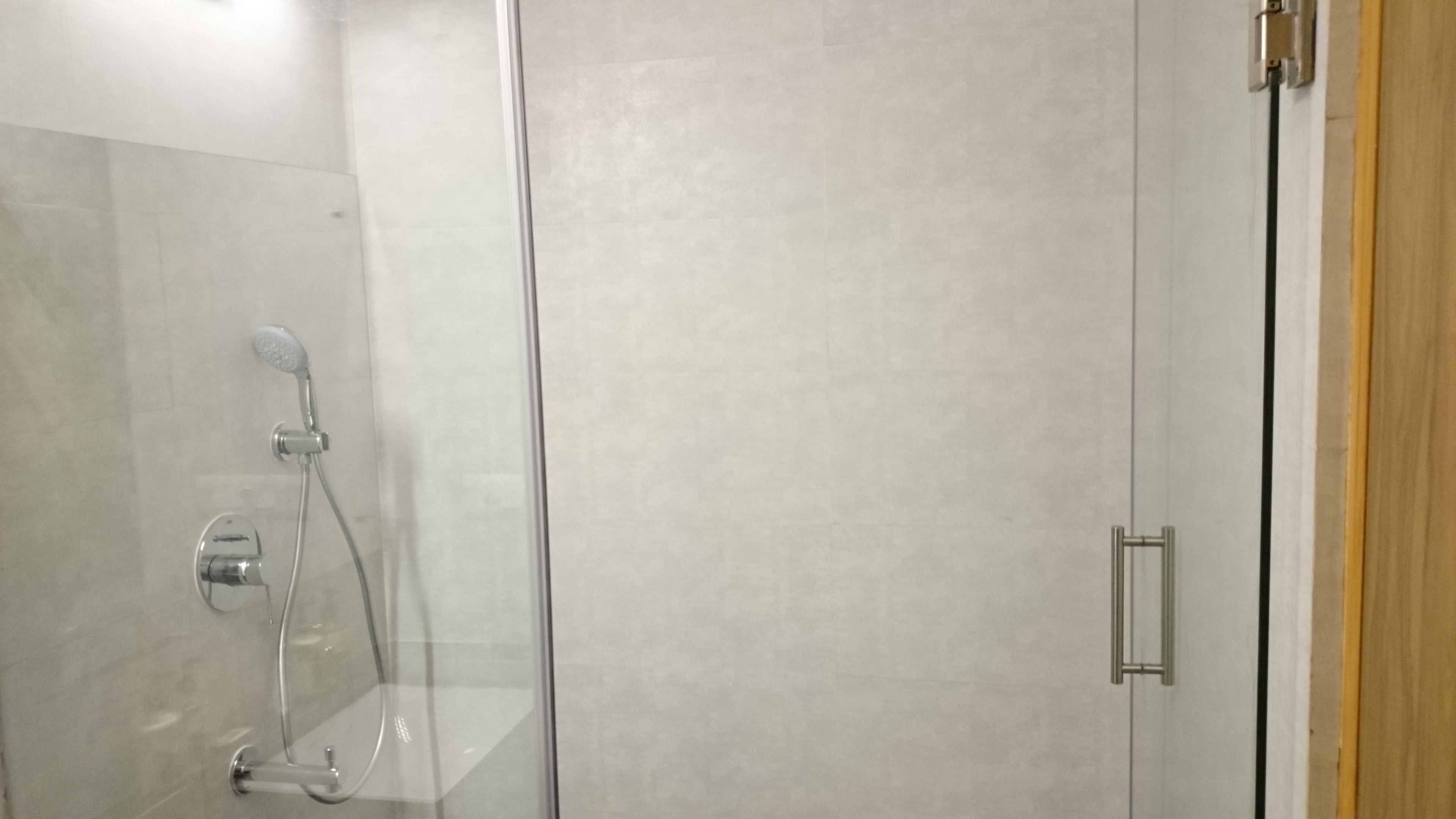Une douche fermée par des parois en verre, dotée d’un pommeau de douche à main et d’un robinet mural.