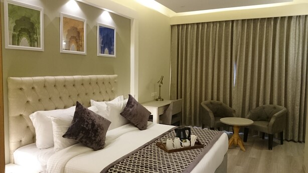 A hotel room with a large bed, two armchairs, a small table, and a desk with a lamp. - Mango Hotels Naveen (Davanagere)