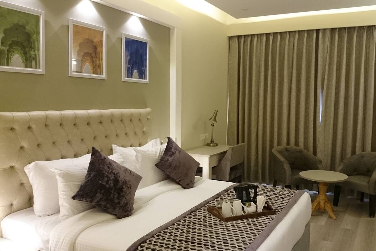 Quarto de hotel com uma cama grande, duas poltronas, uma pequena mesa e uma escrivaninha com abajur.