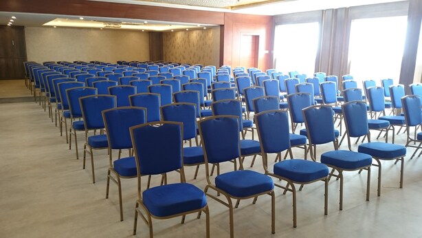 A conference room with rows of blue chairs and a wooden floor. - Mango Hotels Naveen (Davanagere)